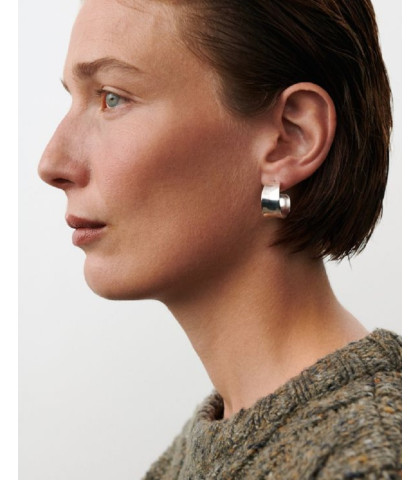 Disse brede, skulpturelle øreringe har et blankt og strålende udtryk, inspireret af vinterlysets klare refleksioner. Designet fremhæver en blød, buet form med rene linjer og en spejlblank overflade, der giver et moderne og sofistikeret look. Perfekte til dem, der ønsker et smykke, der udstråler selvsikkerhed og enkel luksus. Lavet af genanvendt messing belagt med sterlingsølv